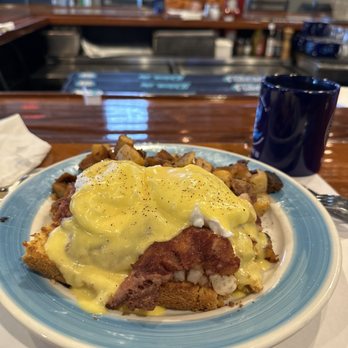 Atlantic Grille - A breakfast dish featuring eggs Benedict topped with sausage gravy, accompanied by breakfast potatoes, on a blue-rimmed plate in a restaurant setting. - Breakfast & Brunch Near Me - Middletown, Rhode Island