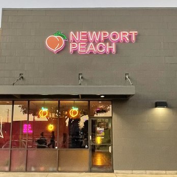 Sign Imaging - Newport Peach's storefront has neon signs with peach imagery and the business name, set against a gray wall with glass windows and a door. - Signmaking Near Me - Bellfower, California