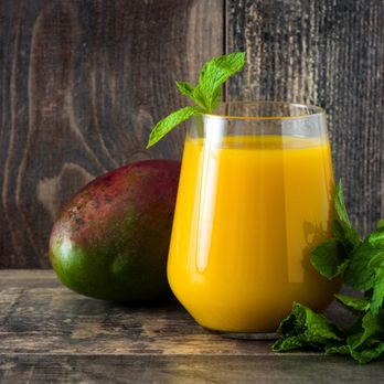 Bayleaf Kitchen - a glass of mango juice next to a mango - Indian Near Me - Klein, Texas