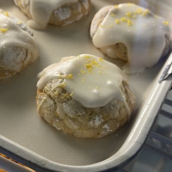 SAP Brunch - Several cinnamon rolls with a golden-brown exterior are topped with white icing and sprinkled with lemon zest. They are arranged on a baking tray, which appears to be in a bakery or display setting. The rolls are freshly baked, with some icing slightly melting into the pastry, and the lemon zest adds a decorative touch. - Breakfast & Brunch Near Me - Appleton, Wisconsin