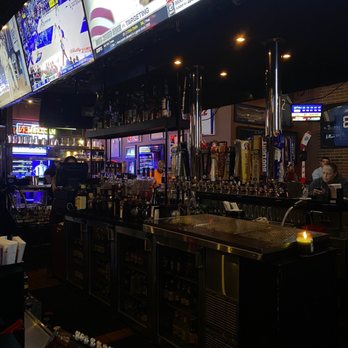 24 Seconds - Main bar - A bar with beer taps, a refrigerated display, and multiple televisions showing sports events, with patrons seated and standing in the background. - Sports Bars Near Me - Berkley, Michigan