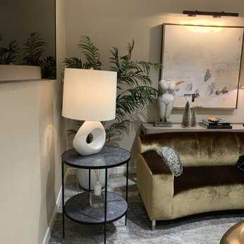 The Rose Clinic - Plastic Surgery in Utah - A cozy living room corner features a lamp with a sculptural base, a velvet sofa, and a side table with decorative objects, including a sculpture and small trees. - Cosmetic Surgeons Near Me - Orem, Utah