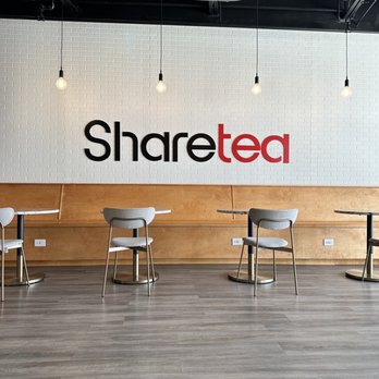 Sharetea - Sharetea's interior features a white brick wall with the logo, four hanging light bulbs, and seating with gray chairs and wooden tables. - Bubble Tea Near Me - Aurora, Illinois