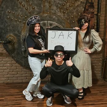 Breakout Studios - Three individuals pose with a whiteboard that reads 'JAK Father of' in an escape room with brick walls and industrial decor. - Escape Games Near Me - San Jose, California
