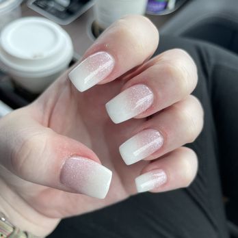 Ava Nails - SNS French Ombré - A hand with manicured nails displays a white French ombré nail design with subtle glitter, held in front of a car interior with coffee cups and medication bottles. - Nail Salons Near Me - Manassas, Virginia