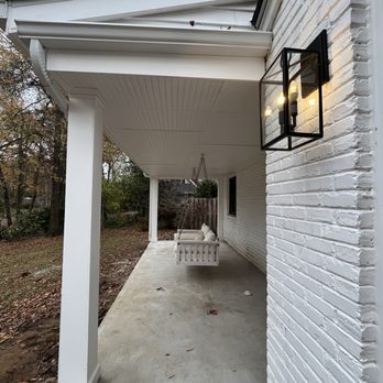 J&D Carpentry - 11-29-24 - A porch with a white ceiling, brick and white painted walls, and a hanging swing with cushions, adjacent to a garden area. - General Contractors Near Me - Manassas, Virginia
