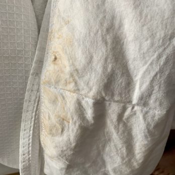 Hyatt Place Phoenix - Filthy coverlet that was not replaced. Stain hidden by housekeeping by rotating to foot of bed. - The image depicts a crumpled white fabric or paper material with visible stains, discoloration, and creases. The material appears to be part of bedding or a cover, with some areas showing yellowish or brownish stains. The background includes textured fabric and a wooden surface, suggesting an indoor setting. - Venues & Event Spaces Near Me - Phoenix, Arizona