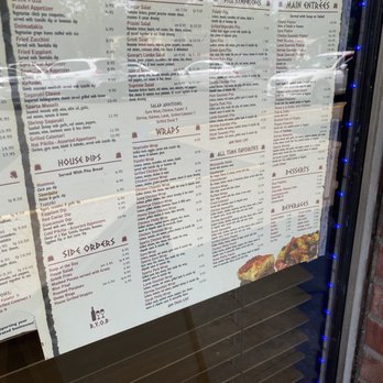 Cedar Tree - A menu board on a restaurant window lists Greek salads, wraps, main entrees, sides, and desserts with prices, featuring Mediterranean cuisine options. - Mediterranean Near Me - River Vale, New Jersey