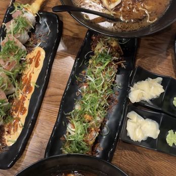 Daruma - Creamy Albacore Roll Vegas Roll Black Mayu Tonkotsu Ramen - A variety of Japanese cuisine is displayed, including ramen bowls with toppings and sushi rolls garnished with green onions, served on black plates. - Ramen Near Me - Mesa, Arizona