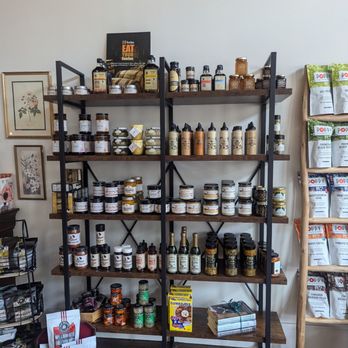 The Gracious Table - Rubs, marinades, dips...etc - Wood and metal shelving units display jars, bottles, and food items, with additional products on a side rack and a bag display to the right. - Used, Vintage & Consignment Near Me - Somerset, Kentucky