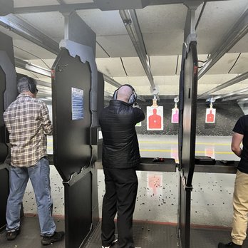 RTSP - Three individuals are at an indoor shooting range, aiming at targets with safety gear, including ear protection, visible in the image. - Gun/Rifle Ranges Near Me - Randolph, New Jersey