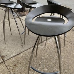Outdoor seating with black modern chairs featuring circular cutouts and metal legs, placed on a sidewalk near a tree.