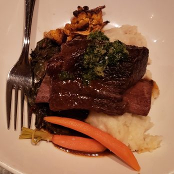 Revival Bar & Kitchen - braised short ribs ($31) - so tender, very good - A plate features braised short ribs topped with sauce and herbs, accompanied by mashed potatoes, carrots, greens, and roasted cauliflower. - New American Near Me - Berkeley, California
