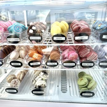 LOVELY MACARONS - Variety is life! - A glass display case contains multiple rows of macarons in different colors and flavors, labeled with tags such as 'Birthday Cake,' 'Cotton Candy,' and 'Lemon.' - Macarons Near Me