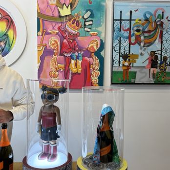 Frame Chicago - A stylized doll wearing sunglasses and boots is showcased in a glass display case, with artwork featuring a crowned figure and children in the background. - Framing Near Me - Chicago, Illinois