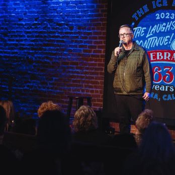 Cool Beans Comedy - my debut at the Ice House after studying with Corey Martin Craig at Cool Beans Comedy ! - A man stands on stage at The Ice House Comedy Club in Pasadena, CA, holding a microphone during a stand-up comedy performance with a brick wall background. - Performing Arts Near Me - Pasadena, California