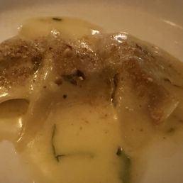 Short Ribs - A close-up of homemade ravioli filled with short ribs meat, served in a creamy sauce with herbs, on a white plate.