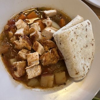 Blue Heron Restaurant - Green chili stew - A bowl of green chili stew with diced chicken, potatoes, and a flour tortilla on the side, served in a restaurant setting. - New American Near Me - Santa Fe, New Mexico