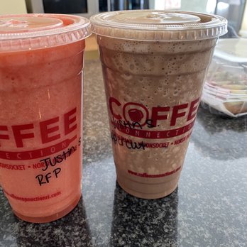 Coffee Connection - Rainforest punch fruit smoothie, upper cut protein smoothie - Two iced coffee beverages in clear plastic cups with red branding are placed on a granite countertop, with a kitchen background. - Coffee & Tea Near Me - North Attleborough, Massachusetts