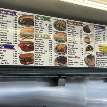 Ted's Burgers - A menu board at Ted's Burgers in Carson, CA, displays food categories including sandwiches, salads, side orders, Mexican food, and beverages. Items listed include cheeseburgers, salads, fries, tacos, and drinks, with prices shown for each. The board is mounted above a stainless steel counter, with a fluorescent light fixture illuminating the menu. The layout is organized into sections with colorful headings and images of some dishes. - Burgers Near Me - Carson, California