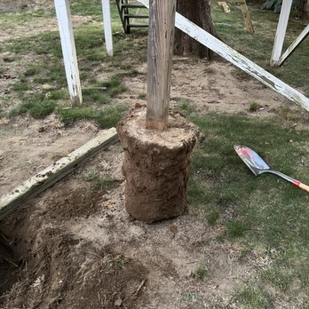 Junk King Rhode Island - A tree is stabilized with a wooden post and a large dirt block in a backyard with a wooden fence and playground equipment. - Junk Removal & Hauling Near Me - Cranston, Rhode Island