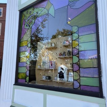 HausWitch - Outside - Stained glass window with abstract, colorful designs, reflecting trees and buildings outside, showing a shop interior with shelves and merchandise. - Spiritual Shop Near Me - Salem, Massachusetts