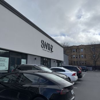 Sweathouz - Exterior - A commercial building with a sign 'SWITZ Contrast Therapy Studio' is shown with several parked cars in front, under a cloudy sky. - Saunas Near Me - Chicago, Illinois