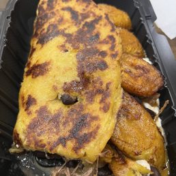 King - A Venezuelan-style arepa with a crispy, golden-brown surface is shown in a black plastic takeout container, with some filling visible underneath.