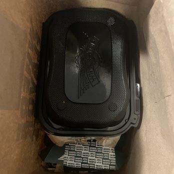 Wingstop - Packaging inside of bag - A black motorcycle saddlebag featuring a logo is positioned inside a cardboard box, with packing paper around it for protection. The saddlebag appears to be made of durable material and has a textured surface with a logo embossed on the top. The box is partially open, revealing the saddlebag and some packing material, indicating it is packaged for shipping or storage. - Chicken Wings Near Me - Albany, New York