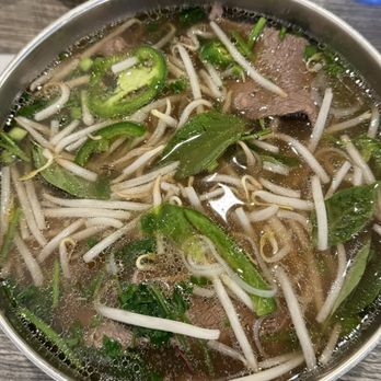 Pho Minh - #102. Pho Filet Mignon Soup - A bowl of Vietnamese pho containing beef slices, bean sprouts, and fresh herbs, served on a wooden table with side condiments and utensils. - Soup Near Me - Temecula, California