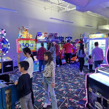 KidMania - A spacious indoor arcade area with children and adults engaging with arcade games, featuring colorful lighting and a patterned carpet. - Arcades Near Me - Plano, Texas