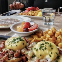Meaty eggs benedict with breakfast potatoes and a pancake.