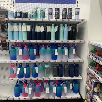 Five Below - The image features a retail display shelf at Five Below in Albuquerque, NM, filled with an assortment of reusable water bottles and tumblers. The bottles are arranged in multiple rows, with colors including blue, pink, black, and clear, and sizes varying from small to large. Each item has a price tag of $5, and the display is part of a promotional section encouraging online shopping and app use. To the right, part of another shelf with toys is visible. The background includes a sign promoting the store's website and app. - Discount Store Near Me - Albuquerque, New Mexico