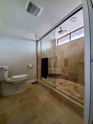 Custom Walk-in Shower Remodel - This custom walk-in shower remodel transforms the bathroom into a spa-like retreat, featuring authentic travertine stone tiles in warm beige tones that cover the walls, floor, and built-in bench for a seamless, natural aesthetic. The enclosure includes a frameless glass sliding door for easy access and a modern, airy feel, complemented by recessed niches for convenient storage of toiletries. A rainfall showerhead, brushed nickel fixtures, and a corner seating bench enhance functionality and comfort, while the overall design integrates harmoniously with the adjacent space, including a window for natural light and subtle accents like diamond-patterned borders. This project emphasizes durability, elegance, and timeless appeal using high-quality, real travertine throughout.
