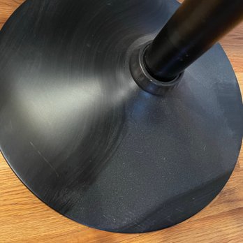 Spotlesstaff - Dust - A black, circular table base with a central support pole is placed on a wooden floor, showing surface scratches and a matte finish. - Home Cleaning Near Me