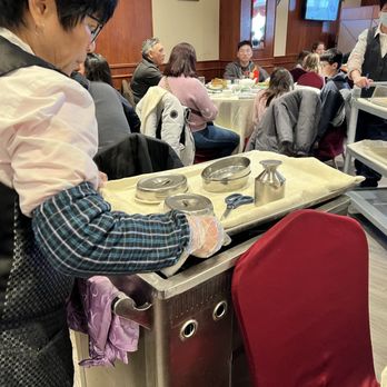 Dim Sum King - A server is setting up utensils and dishes at a restaurant with multiple tables and diners, some wearing masks. - Dim Sum Near Me - Toronto, Ontario