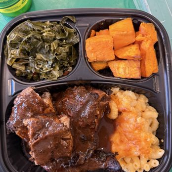 Jerk'D - Jerk chicken bowl - A divided black plastic tray contains collard greens, roasted sweet potatoes, braised meat with gravy, and macaroni and cheese, served with a lemon-lime soda. - Caribbean Near Me - Hackensack, New Jersey