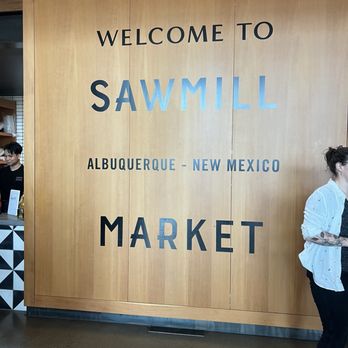 Tulipani - Entrance - A large wooden wall features a sign that reads 'Welcome to Sawmill Market' in Albuquerque, New Mexico, with a person partially visible on the right side. - Pasta Shops Near Me - Albuquerque, New Mexico