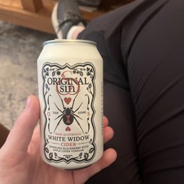 Non-Alcoholic cider option - A hand holds a can of White Widow cider, a non-alcoholic sparkling beverage with blackberry and apple cider vinegar flavor, in an indoor setting.