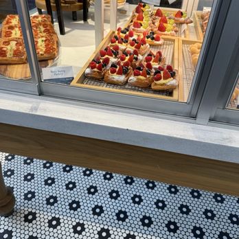 Paris Baguette - A glass display case at Paris Baguette showcases fruit-topped pastries, baked goods, and other desserts, with a black-and-white patterned floor visible below. - Bakeries Near Me - Chicago, Illinois