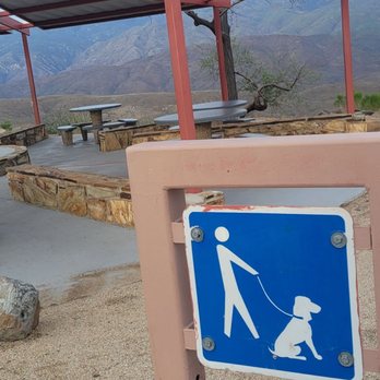 Sunset Point Rest Area - A blue and white sign shows a person walking a dog on a leash at Sunset Point Rest Area, with a picnic shelter and mountain view in the background. - Rest Stops Near Me - Congress, Arizona