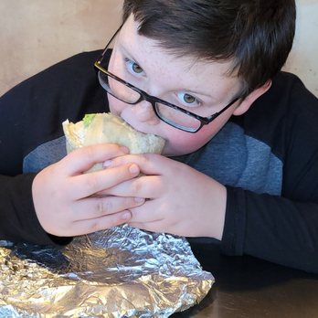 Chipotle Mexican Grill - My Boy - A boy with dark hair and glasses is eating a burrito at a Chipotle restaurant, with a Chipotle napkin on the table. - Mexican Near Me - Schenectady, New York