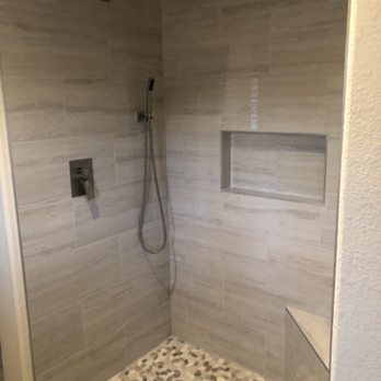 Boonstra Construction, Inc. - a walk in shower - A walk-in shower features beige tile walls, a pebble stone floor, a rainfall showerhead, and a built-in niche for toiletries. - General Contractors Near Me - Oceanside, California