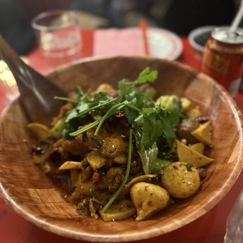 Mala Project - Dry pot - Little Spicy - A wooden bowl holds a mixed Asian dish featuring vegetables, herbs, and possibly tofu or meat, garnished with fresh cilantro. The background includes a glass of water, a red can, and a pink napkin, indicating a dining setting. - Chinese Near Me - Brooklyn, New York