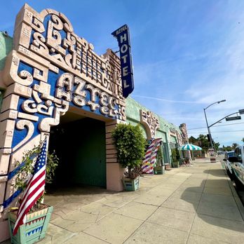 Dulce Cielo - They're located in the historic Aztec Hotel building - A building with a retro design features a large decorative facade with blue and beige accents, and a vertical 'Hotel' sign. The sidewalk has potted plants, umbrellas, and parked cars. - Bakeries Near Me - Monrovia, California