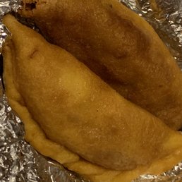 Fried Beef Empanada - Two fried empanadas with golden-brown, crispy crust are shown resting on crumpled aluminum foil. The empanadas are oval-shaped, with one slightly darker in color, indicating they are cooked. The image focuses on the empanadas, which are a traditional dish often filled with meat, cheese, or other ingredients, and are commonly served as street food or in restaurants offering Latin American cuisine.