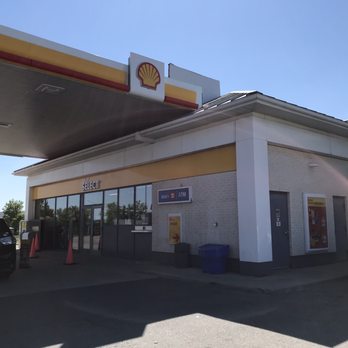 Shell - Storefront - The image shows a Shell gas station located in Markham, ON, with a large canopy displaying the Shell logo and yellow and red color scheme. The station has fuel pumps underneath the canopy, and a storefront with glass doors and windows. There are cars parked near the pumps, and the sky is clear and blue. - Gas Stations Near Me - Markham, Ontario