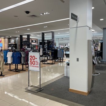 Macy's - Men's - The image shows an indoor clothing store section in a mall, with racks of various apparel including shirts and jackets. A prominent sale sign indicates discounts of 20-50% off storewide. The store has a modern design with bright lighting, and the background includes other retail sections and shoppers. An ATM or kiosk is visible near the entrance, and the flooring is a combination of tile and carpet. - Department Stores Near Me - Columbus, Ohio