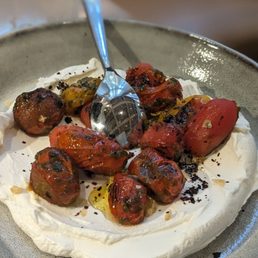 Charred Tomato Labne - Roasted cherry tomatoes with herbs on a bed of creamy cheese, garnished with olive oil and black pepper, served in a bowl.