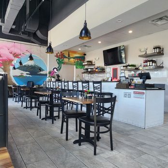 Nori Restaurant - A restaurant interior featuring black chairs, a white bar counter, hanging pendant lights, and colorful murals on the wall. - Asian Fusion Near Me - St. Augustine, Florida